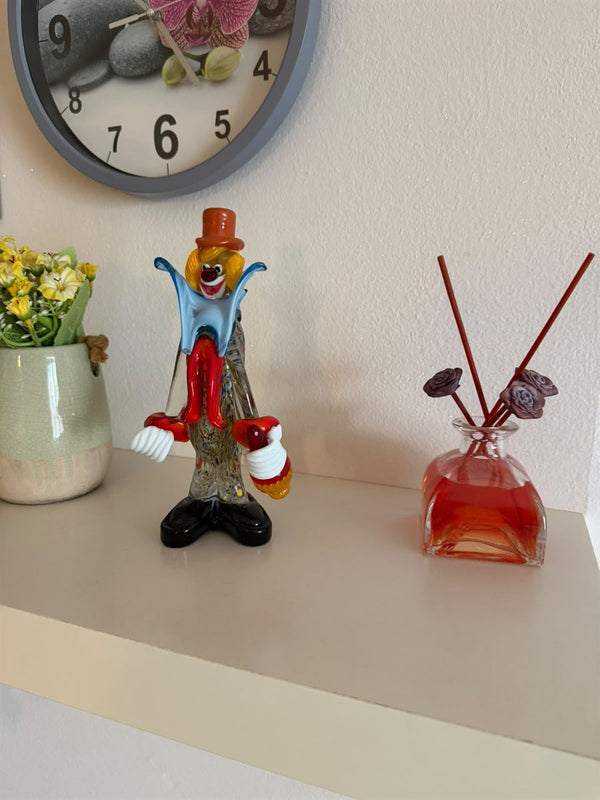 Murano glass clown on a shelf at home, next to a vase of flowers