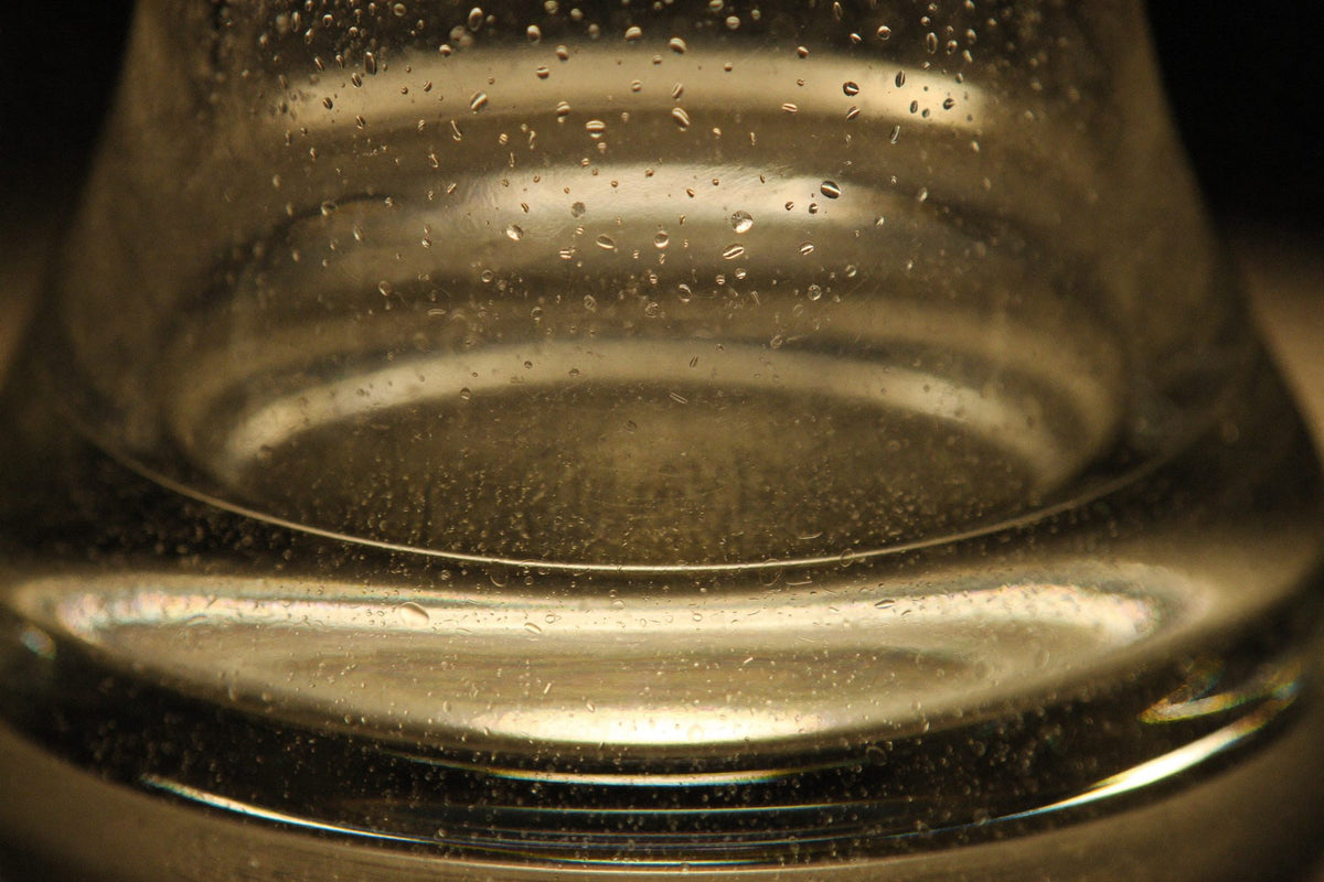 De minuscules bulles d’air dans un verre épais soufflé à la main, à contre-jour